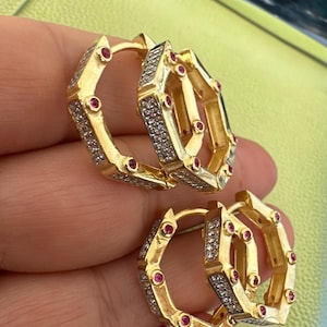 Puede incluir: Pendientes de aro de oro con un diseño hexagonal. Los pendientes están adornados con pequeñas piedras de circonita cúbica transparentes y piedras preciosas rosas.