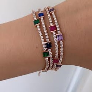 Puede incluir: Una pulsera de oro con múltiples filas de piedras de circonita cúbica transparentes y piedras cuadradas de colores. Las piedras son en tonos de verde, azul, morado y rojo.