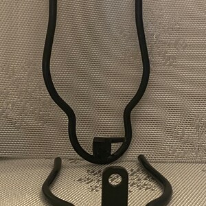 May include: Two black metal bike rack brackets. The brackets are curved and have a hole in the center.