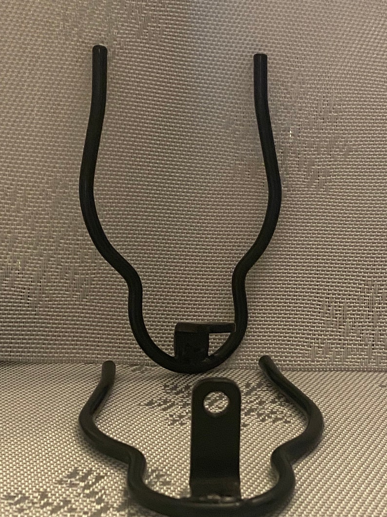 May include: Two black metal bike rack brackets. The brackets are curved and have a hole in the center.