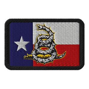 May include: A black and white embroidered patch with a coiled snake with barbed wire and a yellow rattlesnake tail. The snake is on a blue, white, and red Texas flag.