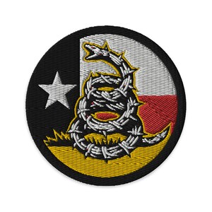 May include: A circular embroidered patch featuring a coiled rattlesnake with a barbed wire design, set against a backdrop of the Texas state flag. The snake is depicted in black and white, with red accents, and is positioned on a yellow field.