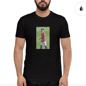 Könnte beinhalten: Schwarzes T-Shirt mit einem Foto eines Fußballspielers, der ein rot-weißes Trikot und schwarze Shorts trägt. Der Spieler geht auf einem grünen Rasen.
