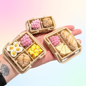 Puede incluir: Mini cestas de comida con cruasanes, huevos, queso y pan. Las cestas beige contienen alimentos rosas, amarillos y blancos. La imagen est&aacute; tomada desde un &aacute;ngulo cercano.