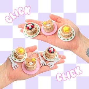 May include: Miniature pancake charms with butter, berries, and bear designs. Each charm is on a small plate and some include a tiny fork. The word "CLICK" is written in pink bubble letters.