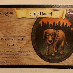 Könnte beinhalten: Eine braune und schwarze Hundekarte aus dem Harry Potter Sammelkartenspiel. Die Karte zeigt eine Illustration eines knurrenden Hundes mit einem Stachelhalsband. Der Kartentext lautet "Surly Hound" und "Damage each turn: 1". Die Karte gehört zur Kategorie "Creature" und ist ein "Dog".