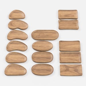 以下が含まれることがあります： さまざまな形とサイズの木製サービングトレイのコレクション。トレイには、楕円形、長方形、フリーフォームのデザインがあり、すべて天然の木目仕上げです。配置はさまざまな形状を示しており、前菜の提供やアイテムの表示に最適です。