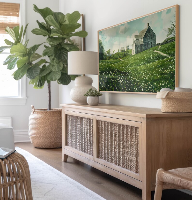 May include: A light wood cabinet with two doors featuring a woven design. The cabinet is sitting on a light wood floor. A large green plant is in a woven basket to the left of the cabinet. A framed painting of a house in a field of flowers is hanging on the wall above the cabinet.