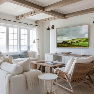 May include: A white living room with a large window overlooking the ocean. The room has a white couch, two white chairs, a wooden coffee table, and a large painting of a green landscape with a house in the distance. The walls are white and the ceiling has exposed wooden beams.