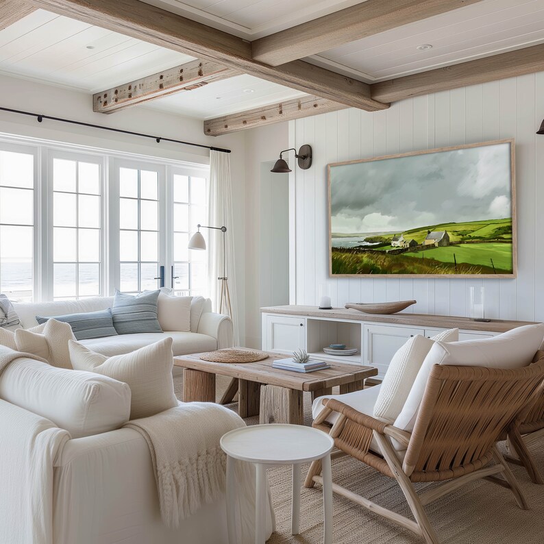 May include: A white living room with a large window overlooking the ocean. The room has a white couch, two white chairs, a wooden coffee table, and a large painting of a green landscape with a house in the distance. The walls are white and the ceiling has exposed wooden beams.