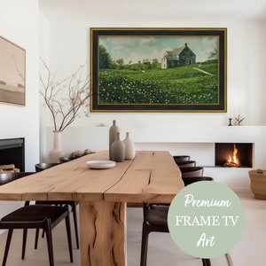 May include: A framed painting of a farmhouse in a field of white flowers. The painting is hanging on a white wall above a wooden dining table with chairs. The table is set with plates and a vase of flowers. The painting is surrounded by a black frame.