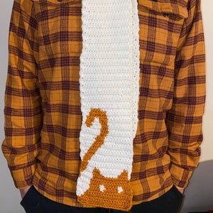 May include: White crocheted scarf with a brown crocheted cat design.