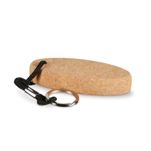Pode incluir: Um porta-chaves de cortiça com uma cor castanha clara natural. A cortiça de formato oval é presa a um cordão preto tecido e a um porta-chaves de metal prateado. O porta-chaves foi projetado para guardar chaves.