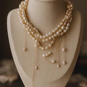May include: A multi-strand necklace featuring cream-colored freshwater pearls interspersed with small gold-toned beads. The design includes several delicate gold chains that drape downward, each ending in a single dangling pearl accent.