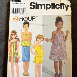 Può includere: Una busta di cartamodello Simplicity per abbigliamento per bambini, taglia AA 3, 4, 5, 6. Il fronte presenta illustrazioni di quattro completi, tra cui un vestito a righe, un top floreale con pantaloni capri, un top giallo con pantaloncini e un vestito floreale.