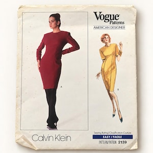 May include: A Vogue Patterns sewing pattern envelope for Calvin Klein design 2139. The front shows two dress variations: a long-sleeved dark red dress labelled A and a short-sleeved yellow dress labelled B. The text includes Vogue Patterns, American Designer, Calvin Klein, and pattern number 2139.