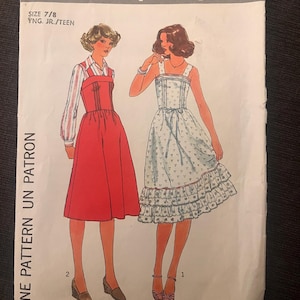 May include: A vintage Simplicity sewing pattern, size 7/8, with two dress designs illustrated on the cover. One dress is red, the other white with a floral print. The text "8049 Simplicity" is at the top of the pattern.