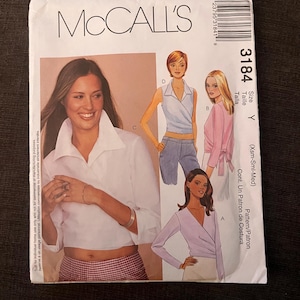 May include: A McCall's sewing pattern envelope with a woman in a white shirt and illustrations of wrap-style tops. The envelope includes the number 3184 and the text "McCall's".