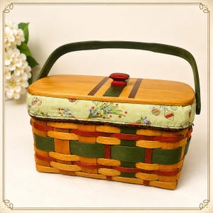 May include: A rectangular woven basket featuring a light wood lid with a red knob and a green handle. The basket body is woven with natural, red, and green strips. A padded fabric border displays a festive pattern of candy canes and ornaments.