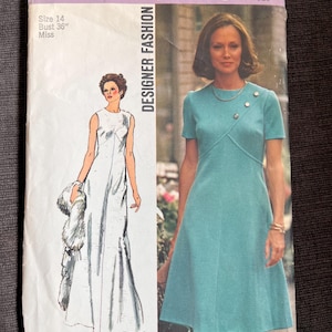 May include: Vintage Simplicity Designer Fashion sewing pattern, size 14, bust 91 cm. The cover features illustrations of two dresses, one long and one short-sleeved, teal-coloured dress. The text includes "5911" and "Designer Fashion".