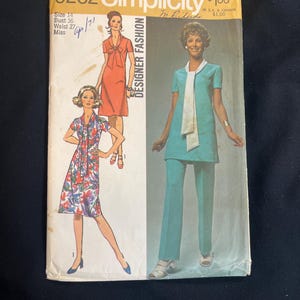 Op de afbeelding: Vintage Simplicity Designer Fashion naaipatroon, maat 14. De omslag toont illustraties van damesoutfits, waaronder een koraalkleurige jurk, een jurk met bloemenprint en een turquoise broekpak. De prijs is $1,00 in Canada.