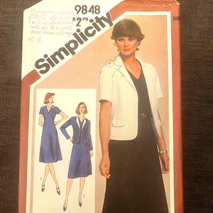 Peut inclure: Une pochette de patron de couture Simplicity 9848 illustrant un ensemble robe et veste. La couverture présente une veste blanche à manches courtes sur une robe sombre, avec des notes manuscrites en haut à gauche et le texte Miss Petite.
