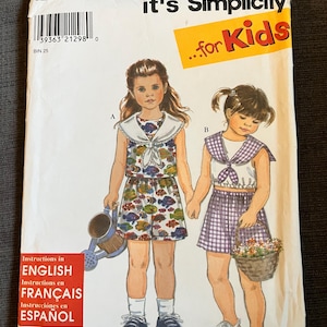Può includere: Una busta per cartamodello Simplicity, numero 8064, taglia A, per abbigliamento per bambini. La copertina presenta illustrazioni di due completi: un set composto da top e pantaloncini con stampa di pesci e uno a quadretti viola.
