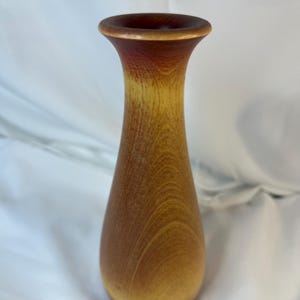 May include: A wooden vase with a light brown to reddish brown gradient. The vase has a narrow opening and a rounded bottom.