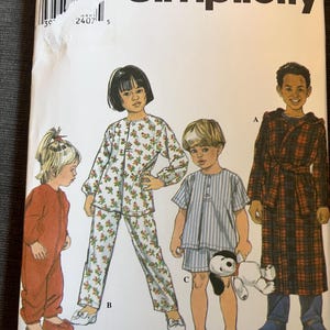 May include: A Simplicity sewing pattern envelope 8493, size BB, featuring illustrations of children's sleepwear. Designs include a plaid hooded robe, a floral long-sleeve pyjama set, a striped short-sleeve pyjama set, and a solid-coloured one-piece sleeper.