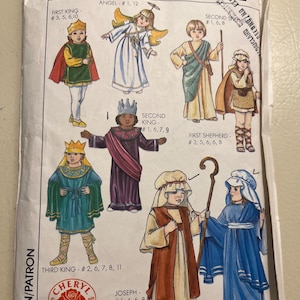 Puede incluir: Sobre de patrón Simplicity con ilustraciones de niños con trajes bíblicos, incluyendo ángeles, reyes y pastores. El paquete incluye la talla LG y el texto "Cheryl Johnson 1988".