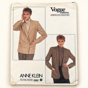 Puede incluir: Un sobre de patrón de costura Vogue Patterns American Designer para una chaqueta Anne Klein, número 2985. El frente presenta dos ilustraciones de una chaqueta en tela beige texturizada, usada sobre una blusa de cuello alto, con bolsillos y mangas largas.