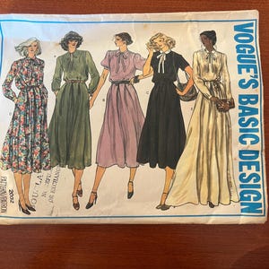 May include: Vintage Vogue's Basic Design sewing pattern envelope. The envelope features illustrations of five different dress designs. The dresses are in various colors and styles, including floral, green, pink, black, and cream. The text "Vogue's Basic Design" is printed on the right side.