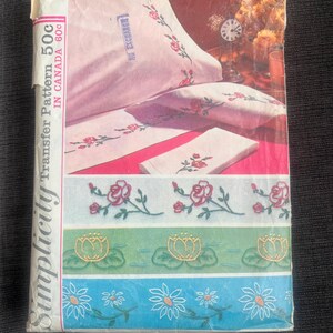 May include: Vintage Simplicity embroidery transfer pattern packet. The packet features a pink and white floral design on a pillowcase and other linens. The packet also shows floral border designs in pink, green, and blue.