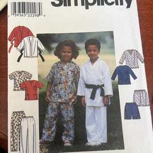 May include: Simplicity sewing pattern 8438 for children's sizes 5, 6, 7, and 8. The envelope features illustrations of various tops and pants, including a white martial arts style uniform with a black belt and a patterned short-sleeve shirt and pants.