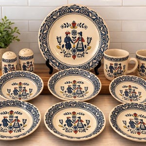 Puede incluir: Un juego de vajilla vintage de color crema con diseños florales y de arte popular azules. El juego incluye un plato grande, cuencos, tazas y saleros y pimenteros. Los platos y cuencos tienen un borde con dibujos azules.