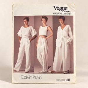 Puede incluir: Un sobre de patrón de costura Vogue Patterns American Designer para el diseño 1508 de Calvin Klein. El frente muestra tres variaciones de prendas blancas: un top de manga corta con pantalón, un top corto sin mangas y una camisa de manga larga.
