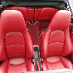 May include: Two red leather seats inside a convertible car. The seats have a smooth, quilted texture and are in good condition.