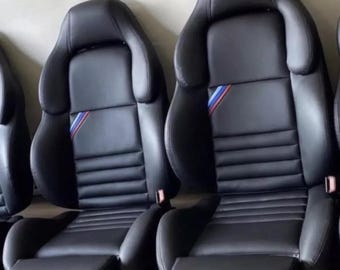 May include: Three black leather car seats with blue, red, and white stripes on the headrest.
