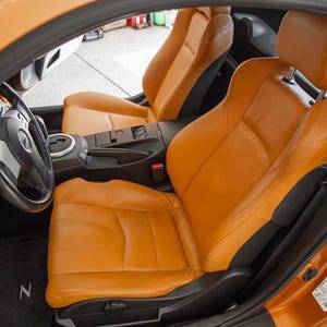Puede incluir: El interior de un coche con asientos de cuero naranja y un volante negro. El coche tiene un salpicadero negro y una alfombra negra con un logotipo "Z".