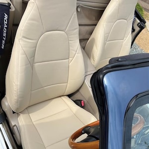 Puede incluir: El interior de un coche descapotable azul con dos asientos de cuero beige y un volante de madera.
