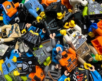 May include: A close-up shot of a pile of colorful Lego minifigure torsos. The torsos are in various colors, including blue, orange, black, and white, with detailed designs. The arms are yellow, and the figures are scattered.