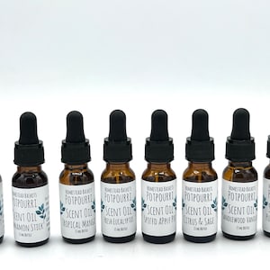 May include: Eight small brown glass bottles with black droppers, each containing a different scented oil. The bottles are labeled with the text "Homestead Baskets Potpourri Scent Oil" and the name of the scent, such as "Watergreen Blast", "Cinnamon Stick", "Tropical Mango", "Fresh Eucalyptus", "Spiced Apple Pie", "Citrus & Sage", "Sandlewood Vanilla", and "Pure Lavender".