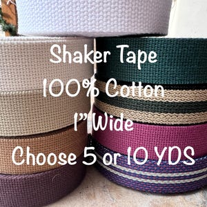 May include: A stack of different colored cotton shaker tapes, each 1 inch wide. The text on the tape reads "Shaker Tape 100% Cotton 1" Wide Choose 5 or 10 YDS".
