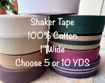 May include: A stack of different colored cotton shaker tapes, each 1 inch wide. The text on the tape reads "Shaker Tape 100% Cotton 1" Wide Choose 5 or 10 YDS".