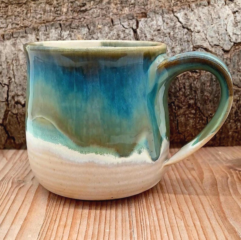 Puede incluir: Una taza de cer&aacute;mica hecha a mano con un esmalte &uacute;nico. La taza presenta un degradado de colores, que va desde una base beige arena hasta una parte superior turquesa y verde azulado. El asa es de color verde azulado a juego. La taza es perfecta para caf&eacute; o t&eacute;.