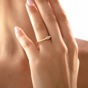 May include: A gold ring with a rectangular design and small, clear stones. The ring is worn on a finger, showcasing its delicate and elegant style. The ring's design is simple yet eye-catching, perfect for everyday wear.