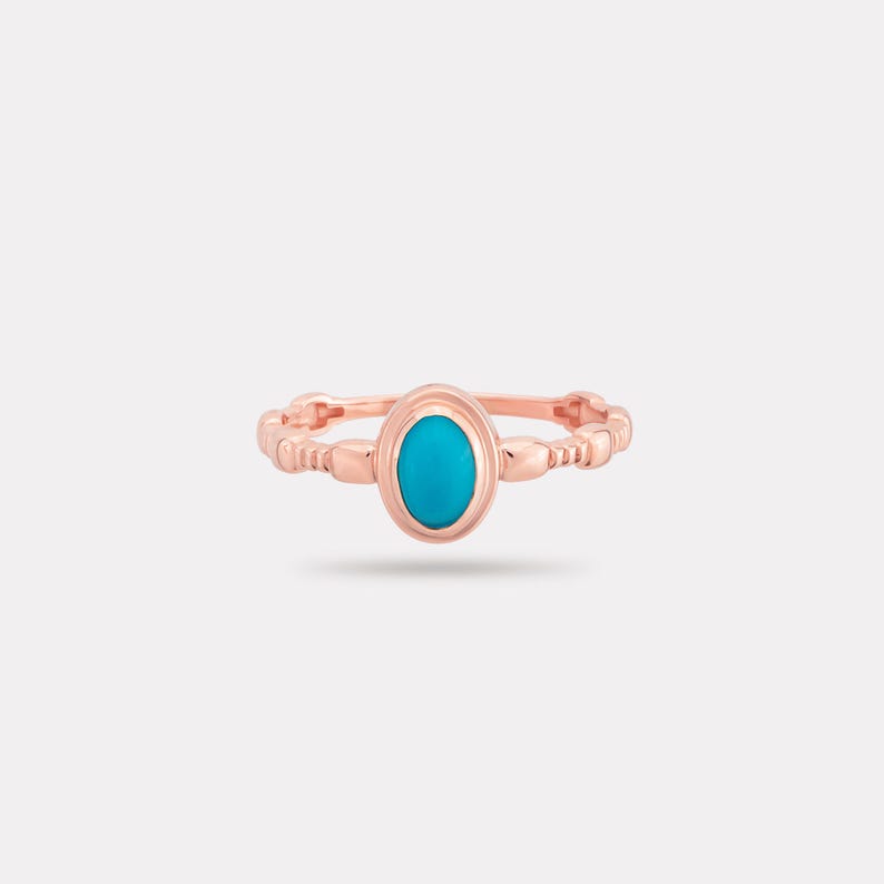 May include: Rose gold ring with an oval, bright turquoise stone. The band has a textured, beaded design. A delicate piece of jewellery.