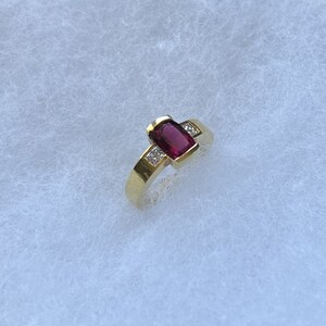 May include: A gold ring with a red gemstone and small diamonds on the band.