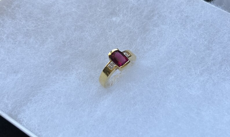 May include: A gold ring with a red gemstone and small diamonds on the band.