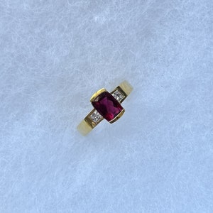 May include: A gold ring with a red gemstone and two smaller diamonds.